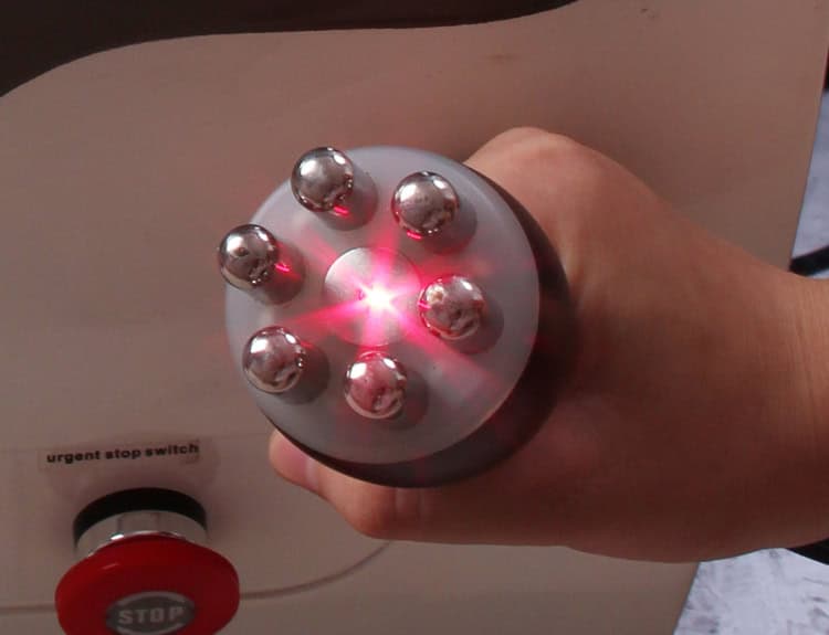 Une personne démontrant la fonctionnalité d'une machine de modelage du corps 6 en 1 Minceur Beauté en maintenant enfoncé un bouton rouge.