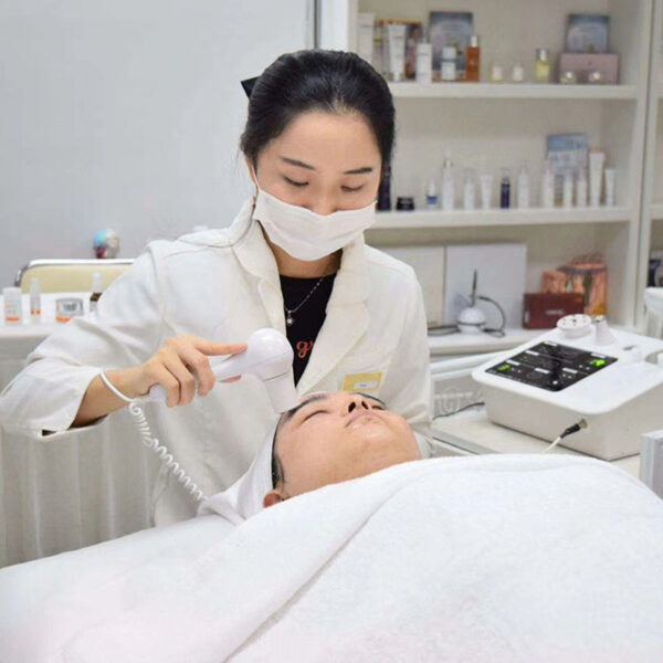 A woman is receiving a Portable Best 3 Handles Microcurrent EMS Electroporation Mesotherapy Stretch Marks Machines facial treatment at a beauty salon, targeting stretch marks.