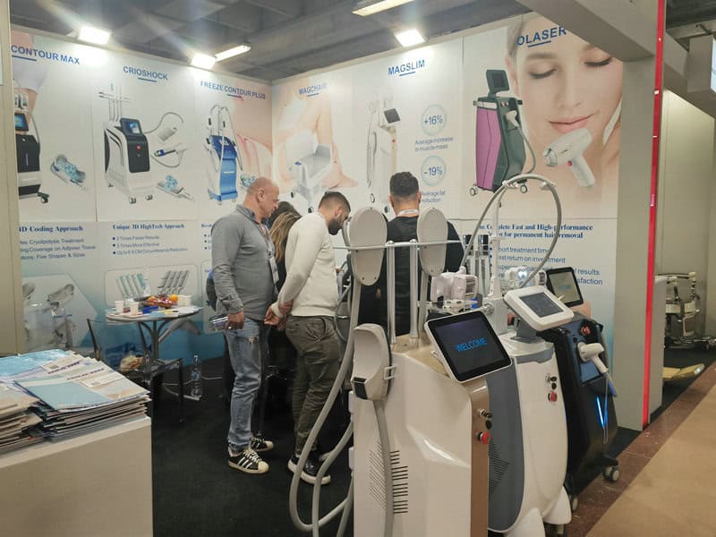 At Cosmoprof 2024 in Bologna, several people examine cosmetic medical devices surrounded by posters on contouring, cryo, and laser treatments.