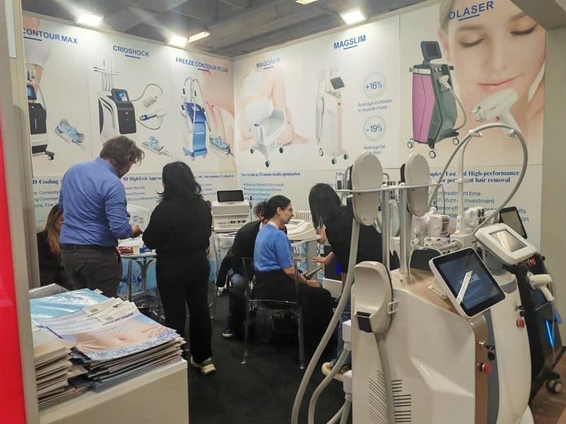 At Cosmoprof in Bologna, a trade show booth features medical aesthetic devices and posters, with attendees standing or seated, discussing.