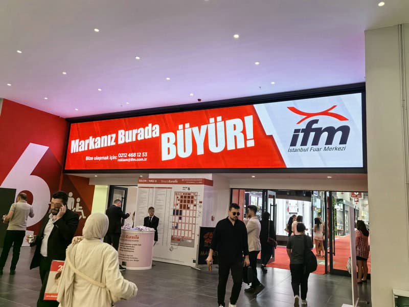 People walk in a convention center lobby under an electronic billboard advertising BeautyEurasia 2024 in Turkish.