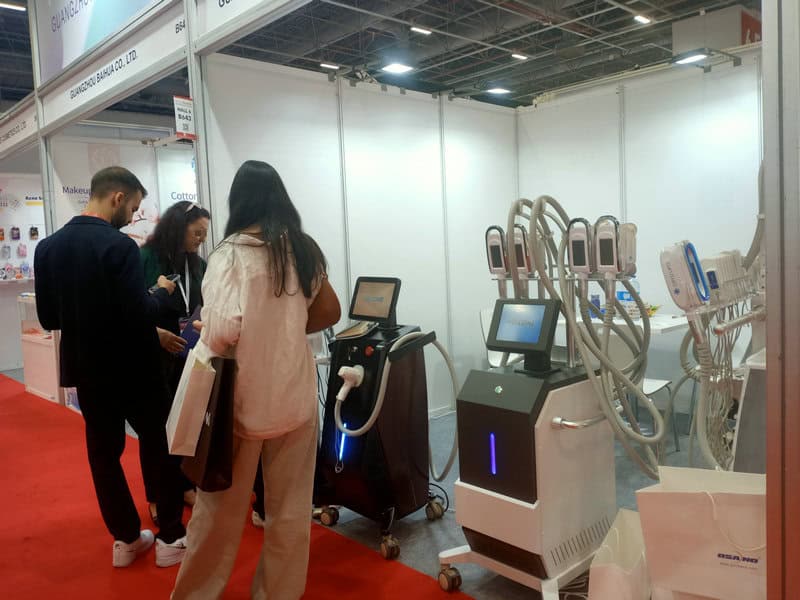 People gather at the BeautyEurasia 2024 booth displaying medical and cosmetic devices with screens and tubes on a red carpeted floor.