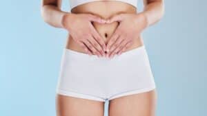 A person in white shorts and a cropped top forms a heart on their stomach, emphasizing safe, non-invasive treatments like laser lipo.