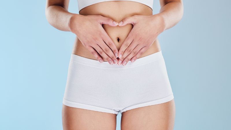 Una persona che indossa pantaloncini bianchi e un top corto forma un cuore sullo stomaco, sottolineando i trattamenti sicuri e non invasivi come la liposuzione laser.