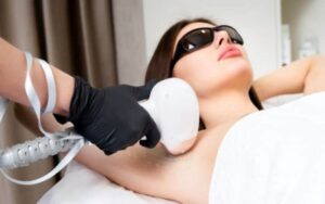 전문 시술자가 레이저 기기를 사용하여 겨드랑이 제모를 하는 동안, 보호 안경을 착용한 여성의 모습입니다.