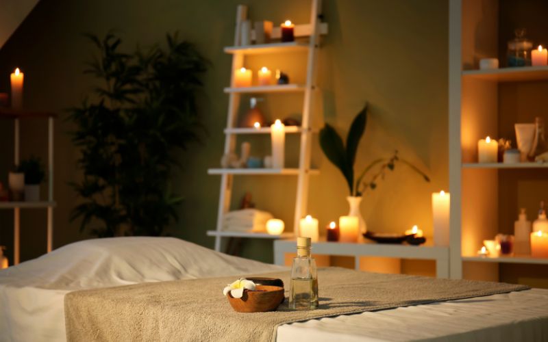 Sala de masajes tipo spa con luz tenue de velas, ambiente relajante, velas suaves y decoración apacible, creando un entorno perfecto para el bienestar y la relajación.