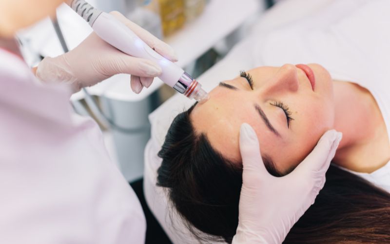Close-up of a woman receiving facial treatment with a skincare device by a professional.