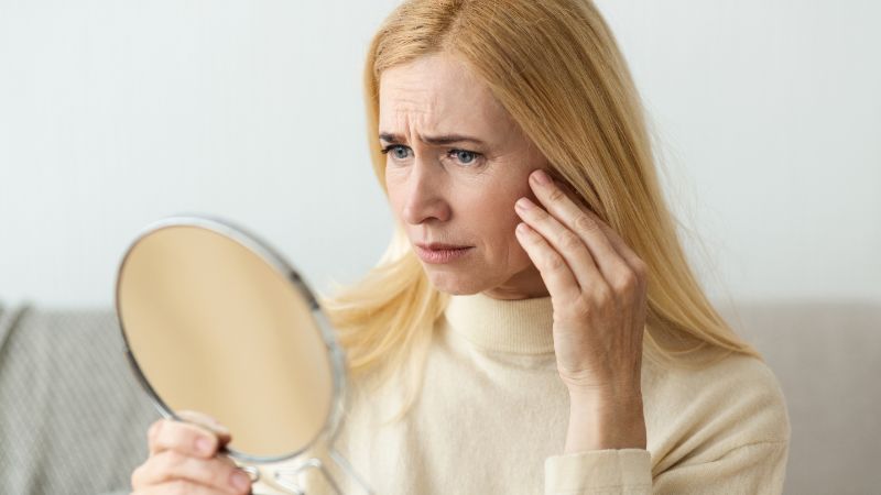 Woman examining her face in mirror, considering Ultherapy treatment for skin lifting and tightening, non-invasive facial rejuvenation.