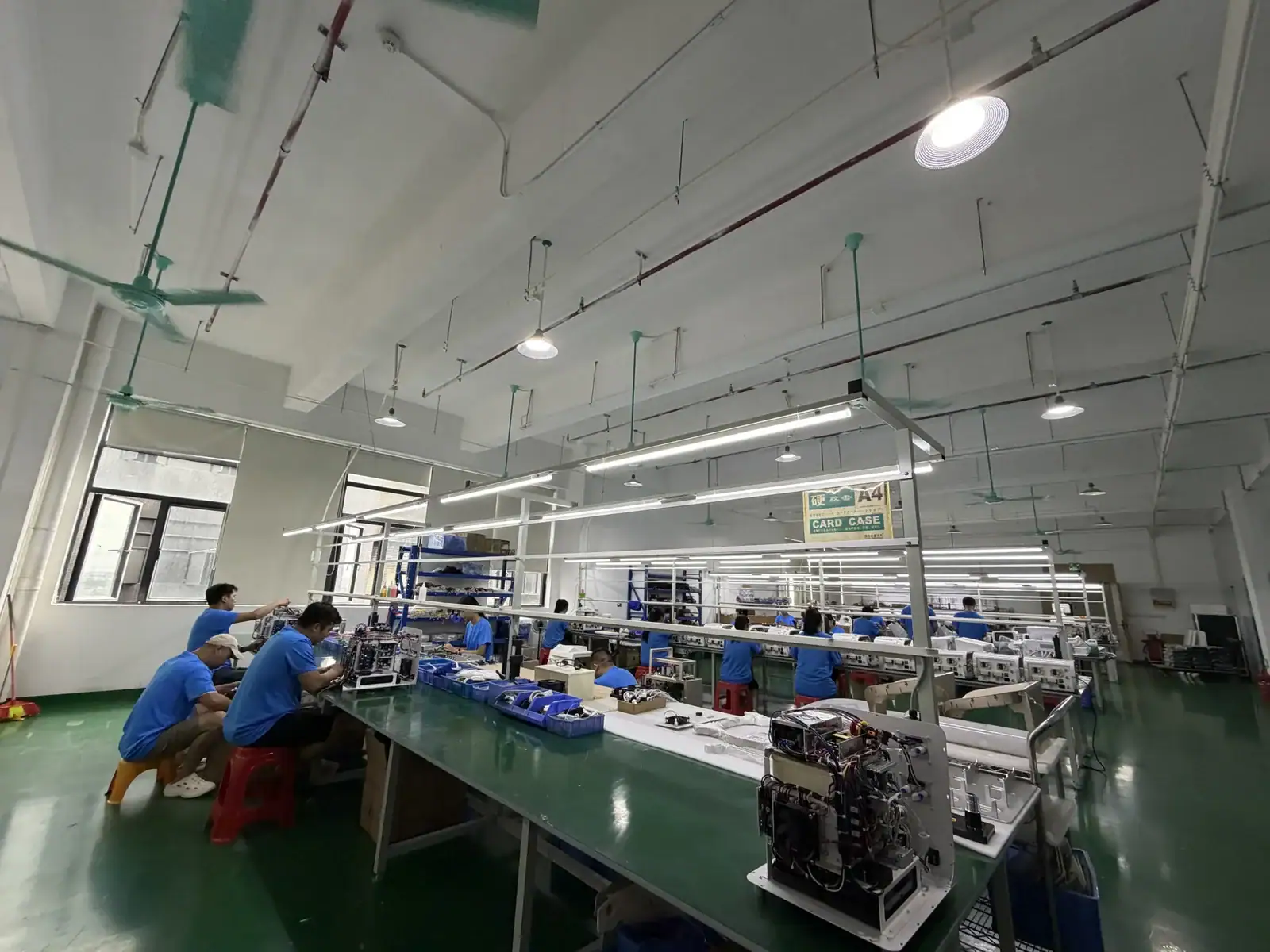 Workers assembling electronic components in a modern manufacturing plant with bright lighting and organized workstations.